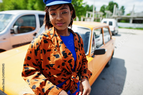Beautiful african american lady with sunglasses standing near orange classic retro car.