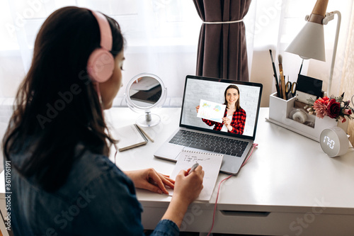 Student learning online. A young girl in a headphone studies remotely online with teacher by video call using a laptop while sitting at home