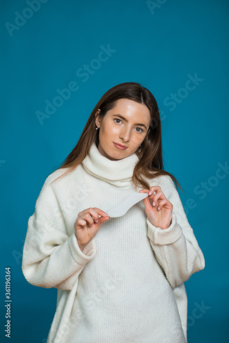 Photo of attractive young lady holds clean sanitary napkin, satisfied with its quality, uses intimate product during menstruation or periods, isolated on blue background