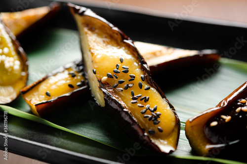 japanese roasted eggplant with miso and sesame on a bamboo leaf on bamboo table mat, closeup