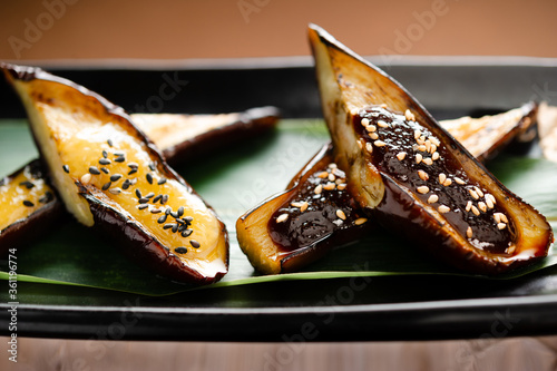 japanese roasted eggplant with miso and sesame on a bamboo leaf on bamboo table mat, closeup photo