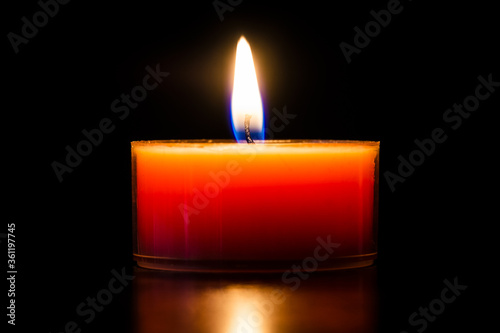 Orange burning candle in a glass tealight beautiful close-up isolated on black.