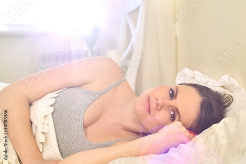 Smiling young woman lying in bed looking at the camera