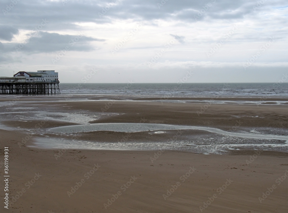 view of the south pier in blackpool with the beach at low tide in front of the sea and a cloudy sky
