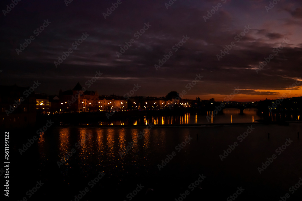 Naklejka premium A view from Charles Bridge where sun sets over the river of Vltava. Reflection of lights and sunset makes the picture perfect.