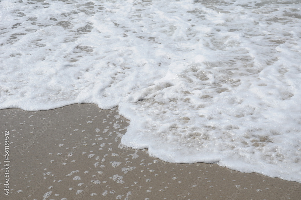 Wave of sea white foam on the sandy shore