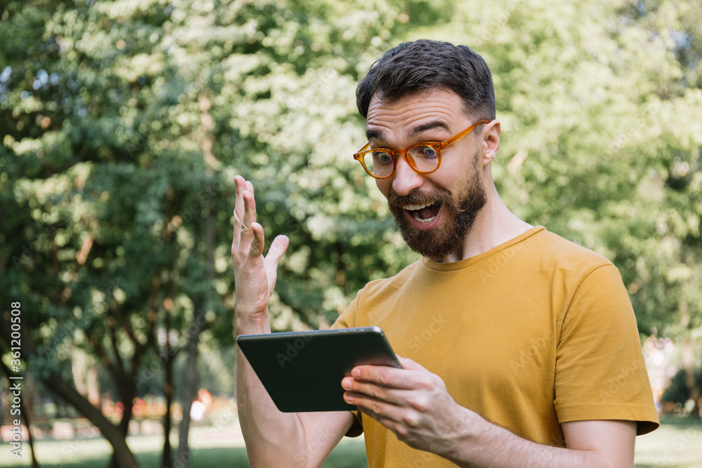 Emotional man using digital tablet, shopping online, watching movie. Excited guy looking at screen, celebration success, sport betting concept Emotional man using digital tablet, shopping online, watching movie. Excited guy looking at screen, celebration success, sport betting concept