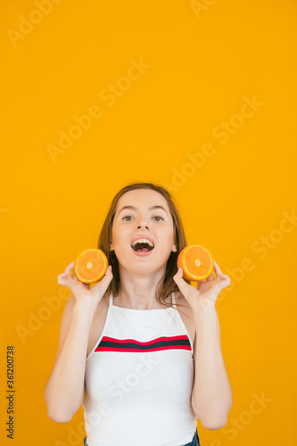 Close up isolated portrait of young woman holding halved oranges at her eyes. Headshot of funny girl wearing white T-shirt. Human face expressions and emotions. Selective focus
