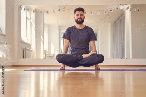 Bearded young man doing lifted lotus or scale pose