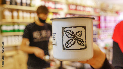Enamel mug hold in hand in the tea shop background. Trade tea concept.