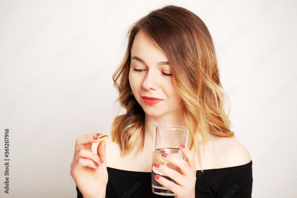 Happy smiling positive woman eating the pill and holding the glass of water in the hand, in her home Happy smiling positive woman eating the pill and holding the glass of water in the hand, in her home