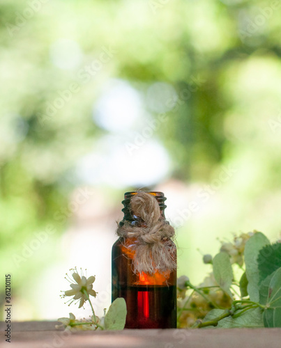 Oil bottle with linden flowers in the blurred nature photo