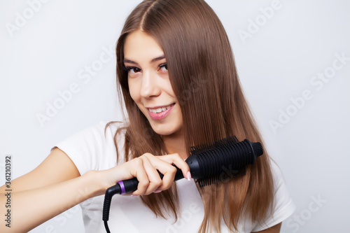 Young woman with luxurious hair straightens it with a curling iron