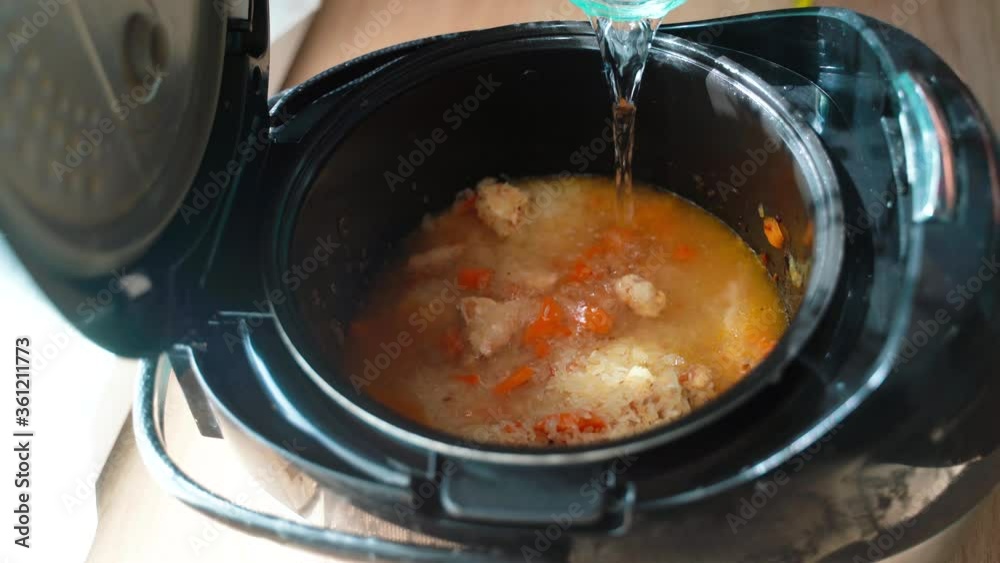 Woman preparing dish and add rice and watter to a dish at home in multicooker. Woman cooks pilaf. Cooking. Delicious dinner. Healthy food. Diet.