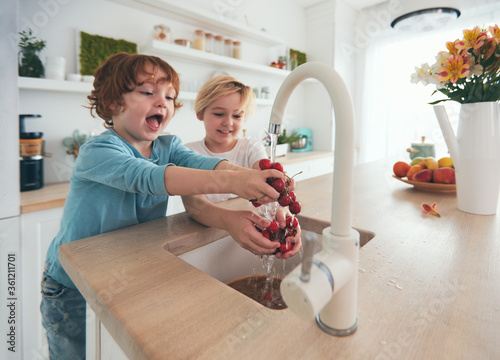 happy kids washing cherries under tap water at the kitchen