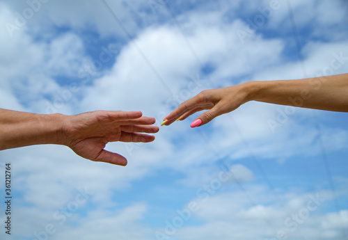 Giving a helping hand. Hands of man and woman on blue sky background. Lending a helping hand. Solidarity, compassion, and charity, rescue. Hands of man and woman reaching to each other, support © Alex