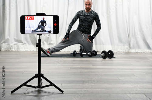 Home fitness workout class live streaming online. Man doing strength training cardio aerobic exercises live on his smartphone for the sportive follower on the social media. Coronavirus - Covid-19.