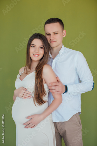Young couple expecting baby standing together on green background. pregnancy, motherhood, people and expectation concept