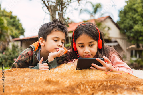 Two kids watching with their smartphones, watching the social media video app, looking at the mobile screen in the garden at home. Siblings share a day outdoors.