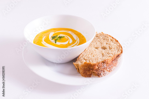 Tigela branca com creme de cenoura no prato branco mais pedaço de pão integral sobre a mesa branca photo