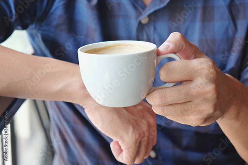 Close-up man hand holding coffee cup foam, hand holding cup of coffee while sitting in cafe 
