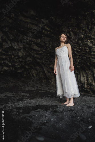 bride in white clothes stands in a black cave on a black sand beach near the Atlantic Ocean in Iceland