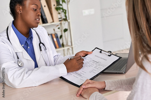 Φωτογραφία Professional medic female african american doctor showing insurance claim form consult caucasian woman explain information to patient at appointment medical visit in clinic