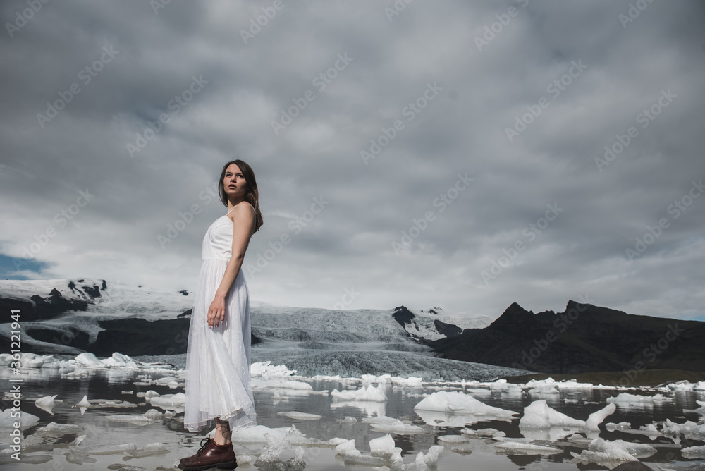 Close-up portrait of a bride in a white dress with a rude make-up. Stands in a field with yellow grass, against the backdrop of a snowy mountain. Destination Iceland wedding.