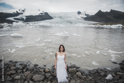 Close-up portrait of a bride in a white dress with a rude make-up. Stands in a field with yellow grass  against the backdrop of a snowy mountain. Destination Iceland wedding.