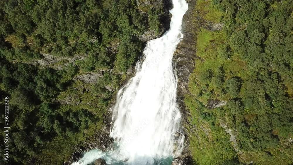 View from above on powerful high waterfall falling from mountain with green forest and rocks. Aerial footage of river of full water in mountains in summer.