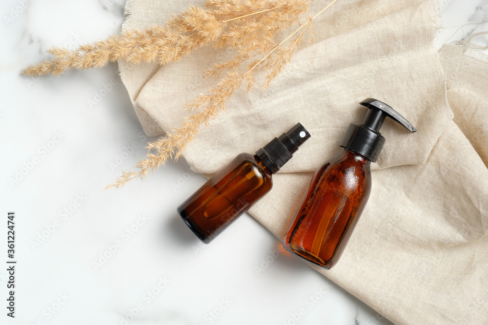 Dark amber glass bottles set with beige fabric and dry flowers on marble background. Luxury beauty products packaging mockups, skin care concept. Dark amber glass bottles set with beige fabric and dry flowers on marble background. Luxury beauty products packaging mockups, skin care concept.