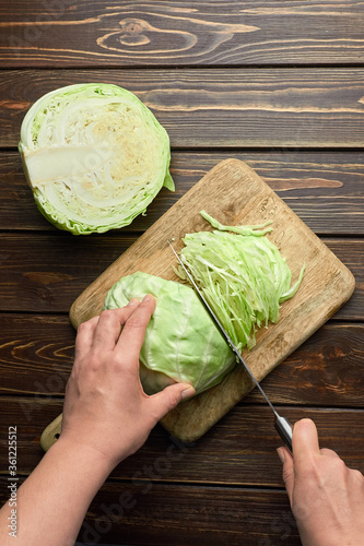 Persons hands chopping fresh cabbage salad over wooden background
