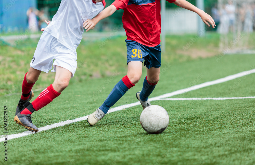 Boys in white and red sportswear plays football on field, dribbles ball. Young soccer players with ball on green grass. Training, football, active lifestyle for kids Boys in white and red sportswear plays football on field, dribbles ball. Young soccer players with ball on green grass. Training, football, active lifestyle for kids