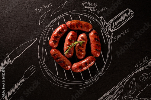 Roasted sausage on black chalkboard with painted pan and ingredients. top view. Barbecue concept. photo