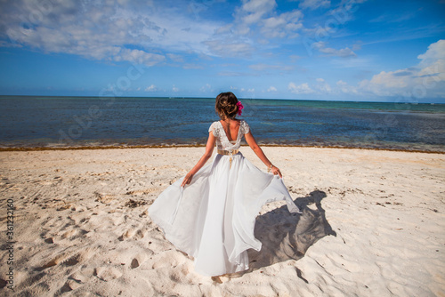 Bride back view in a white wedding dress walking on the sandy caribbean beach landscape on sunny day in Dominican republic 