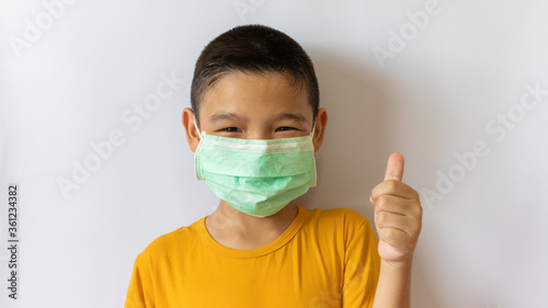 A thai boy wearing a COVID-19 anti-virus mask and dust is pretending to raise his thumb. white background in the house
