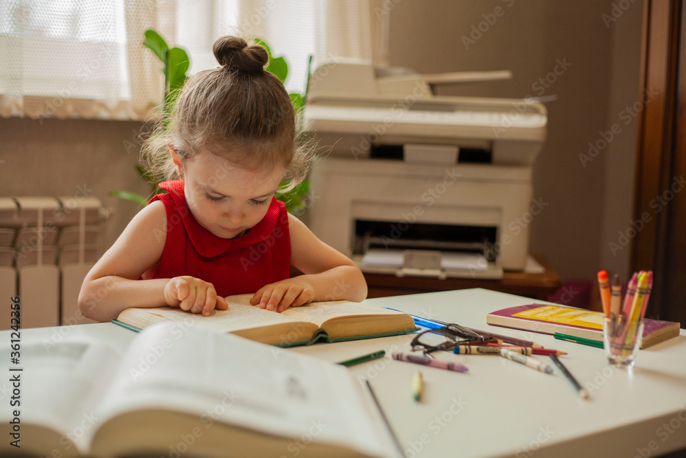 Little girl is reading a book. A girl looks into a book and moves her finger across the text. Preschool education. Education and science. International Literacy Day. Little girl is reading a book. A girl looks into a book and moves her finger across the text. Preschool education. Education and science. International Literacy Day.