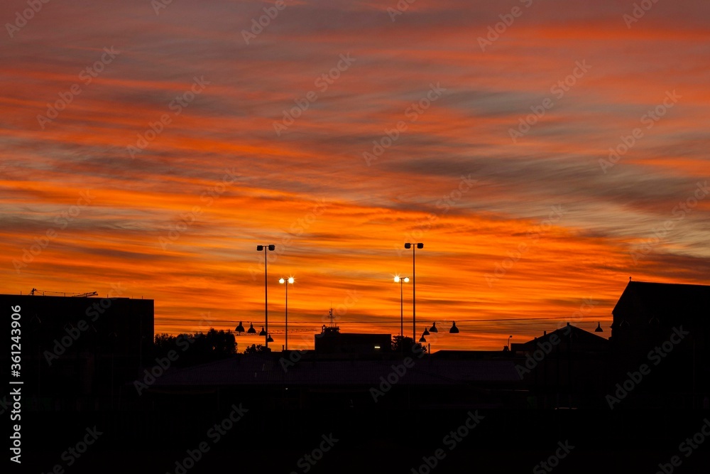 Colourful orange sunset over Perth city, Western Australia, with silhouette buildings and arena lights. 