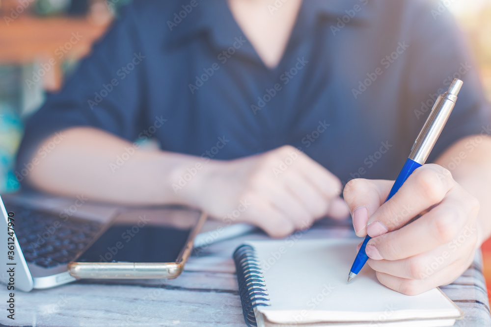 Business woman is writing on a notebook with a pen and using a laptop to work in the office.