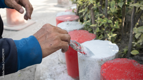 The hand of a man holding the handle to paint the curb White and red. Parking is prohibited in accordance with traffic regulations.