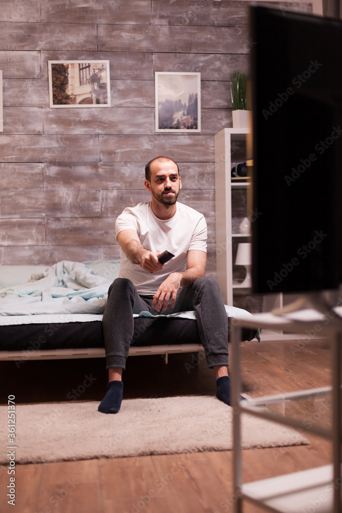 Man sitting on the edge of his bed at night changing channels on tv with remote control. Man sitting on the edge of his bed at night changing channels on tv with remote control.