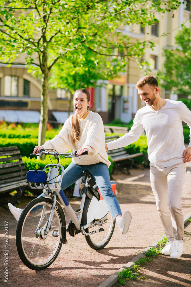 Cheerful woman on bicycle and attentive man running nearby