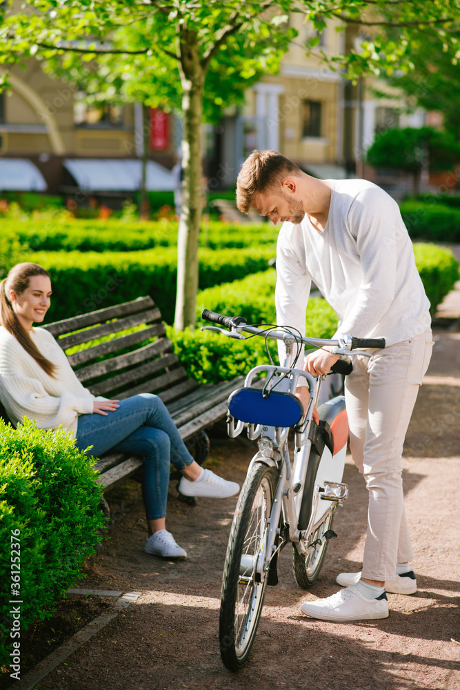 Attentive man inspecting bicycle man and woman on a bench Attentive man inspecting bicycle man and woman on a bench