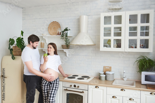 Future parents embrace standing in the kitchen. Pregnant wife gives husband a green apple. Healthy food, Lifestyle, parenthood, motherhood, expectation of a child. Copy space. Family pregnancy concept © MestoSveta