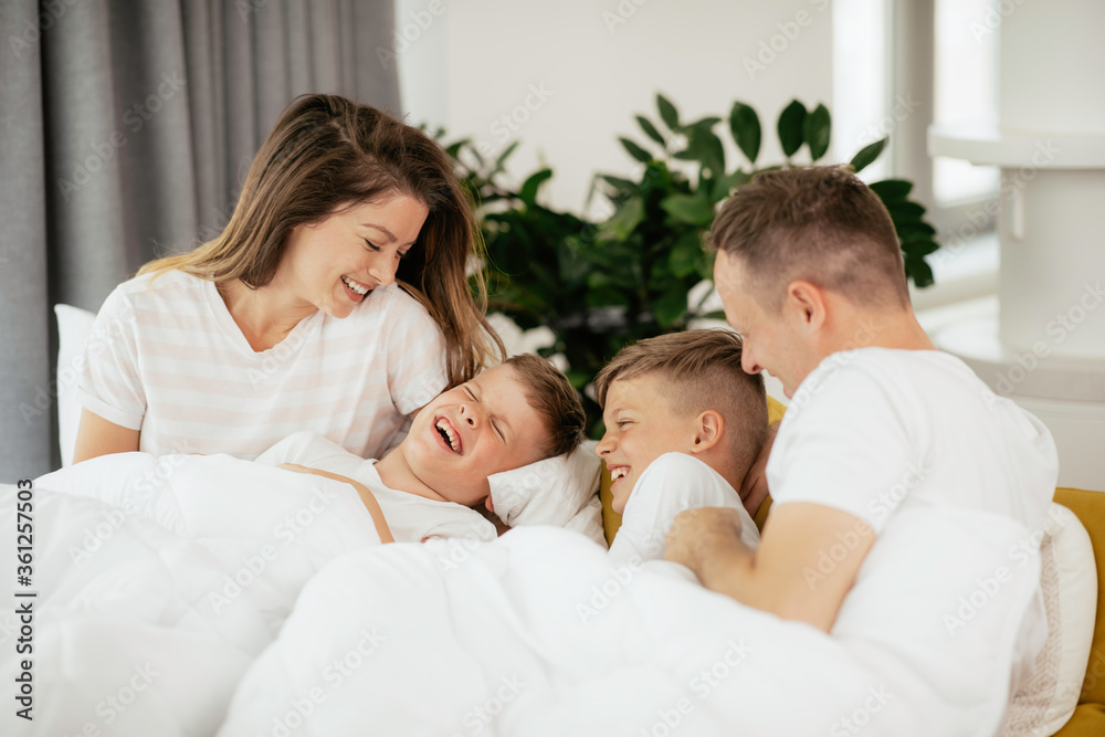 Young family enjoying in bed. Happy parents with sons relaxing in bed.	