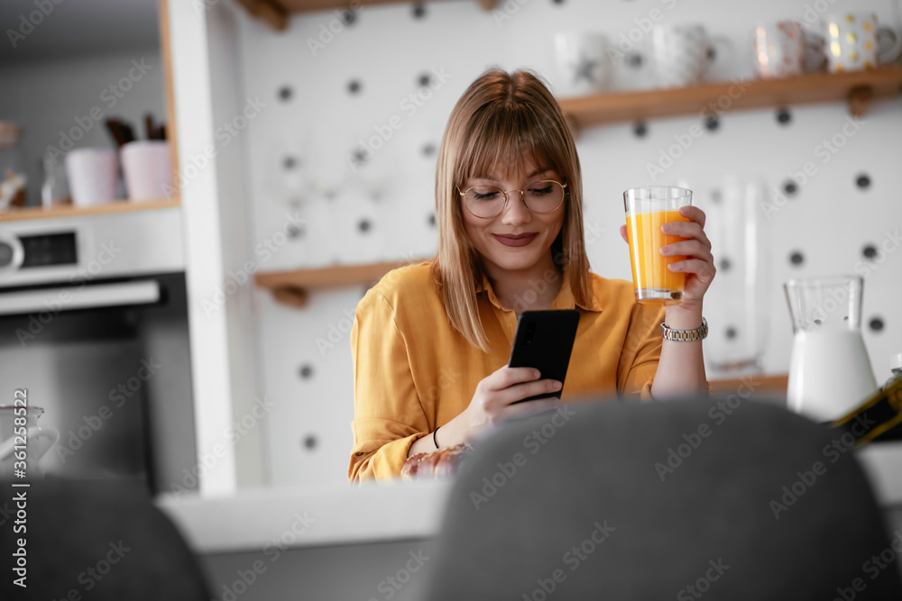 Beautiful woman drinking orange juice in the kitchen. Young woman reading the news online. Beautiful woman drinking orange juice in the kitchen. Young woman reading the news online.