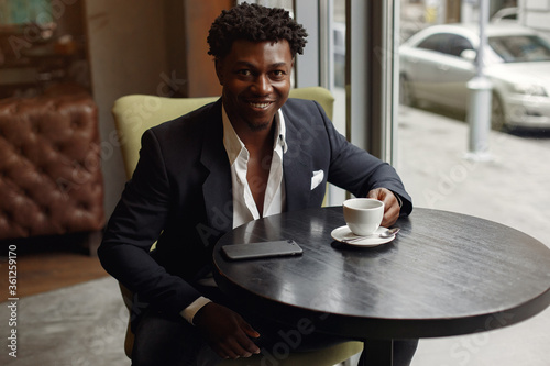 Black man in a cafe. Guy drinking a coffee. Man in a black suit.