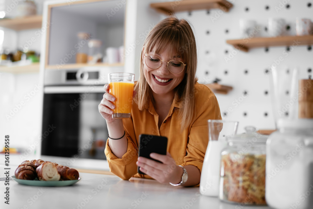 Beautiful woman drinking orange juice in the kitchen. Young woman reading the news online. Beautiful woman drinking orange juice in the kitchen. Young woman reading the news online.