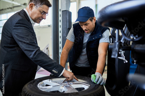 Mid adult manager and mechanic examining car tire in auto repair shop. © Drazen