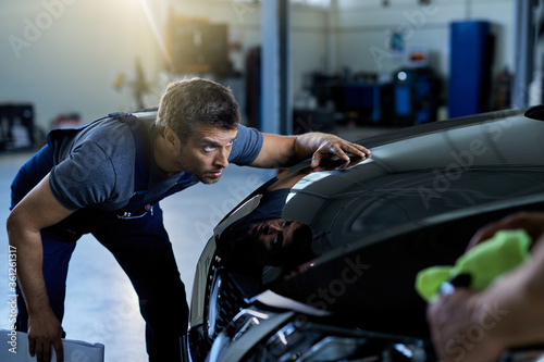 Auto repairman examining vehicle hood in a workshop.